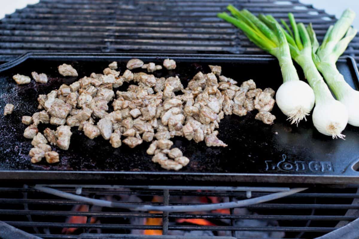 Carne asada and green onions on a flattop grill.