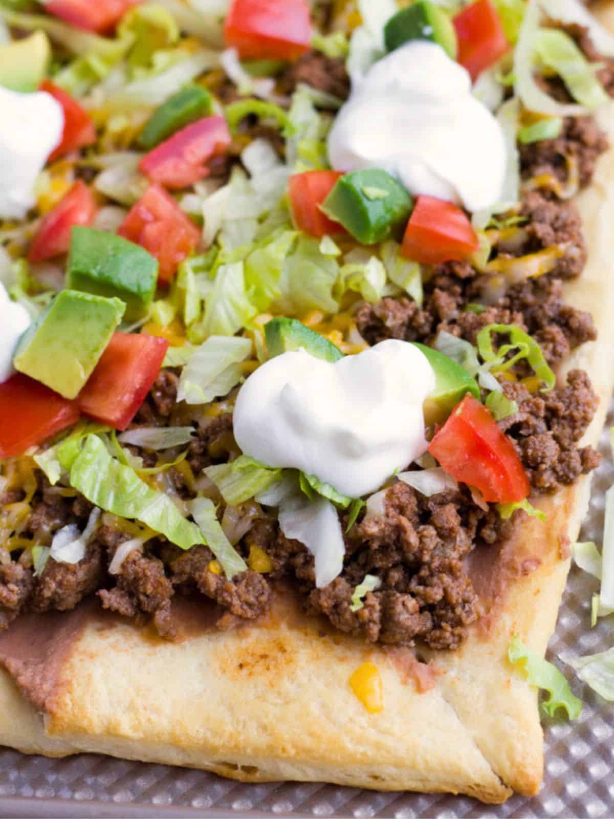 Crescent dough taco pizza topped with meat, lettuce and tomatoes.