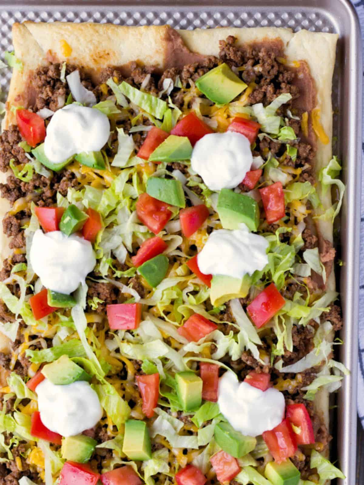 Overhead view of taco pizza with toppings on a baking sheet.