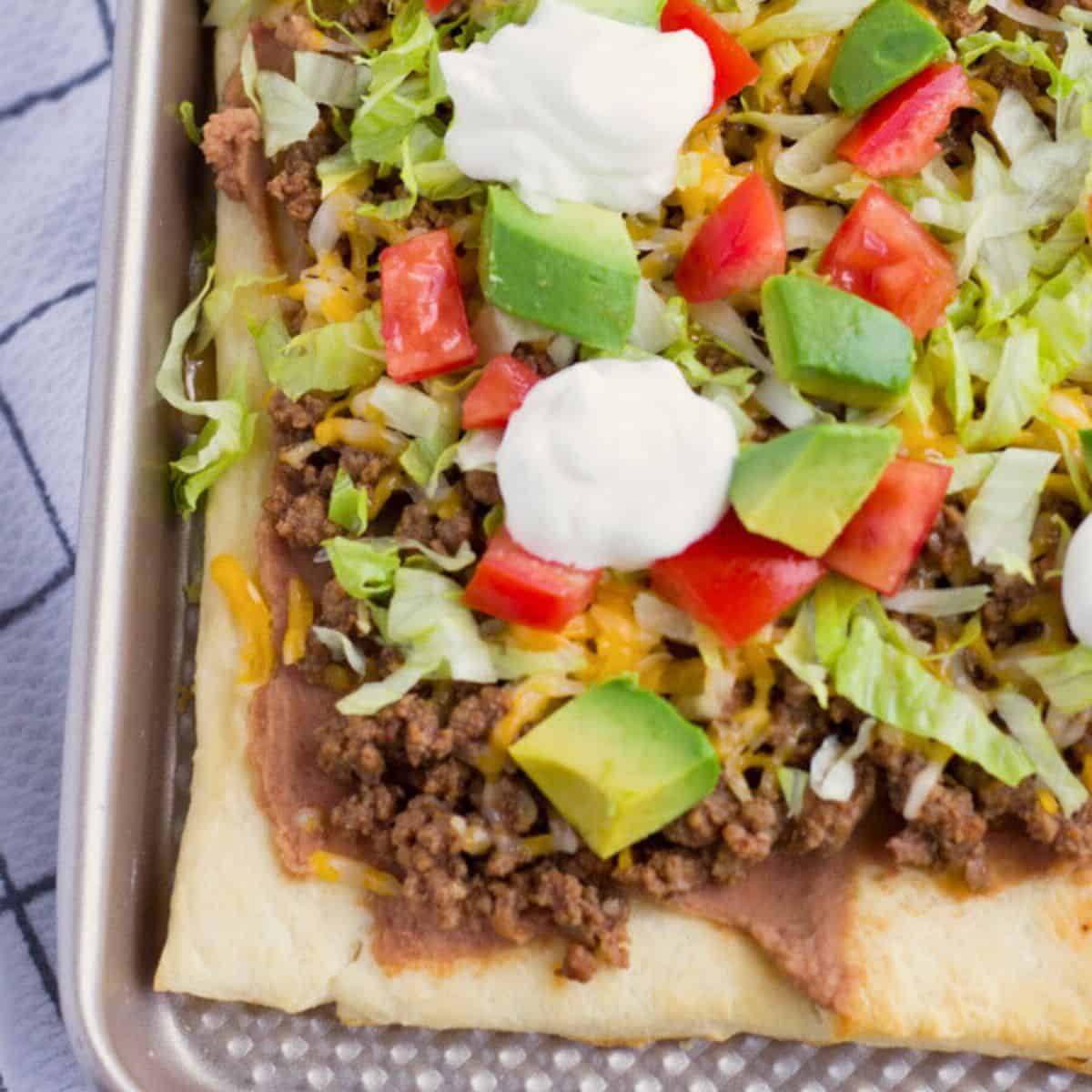Taco pizza with toppings on a baking sheet