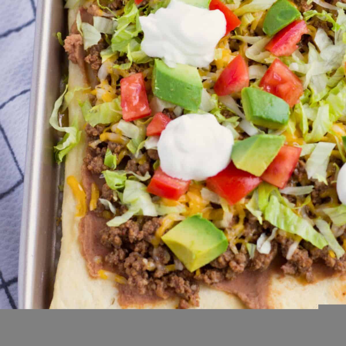 Taco pizza with toppings on a baking sheet