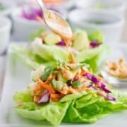 Chicken lettuce wrap with peanut dressing being drizzled on by a spoon.