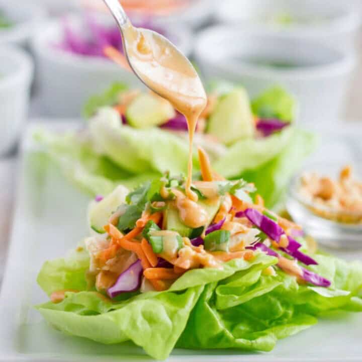 Chicken lettuce wrap with peanut dressing being drizzled on by a spoon.