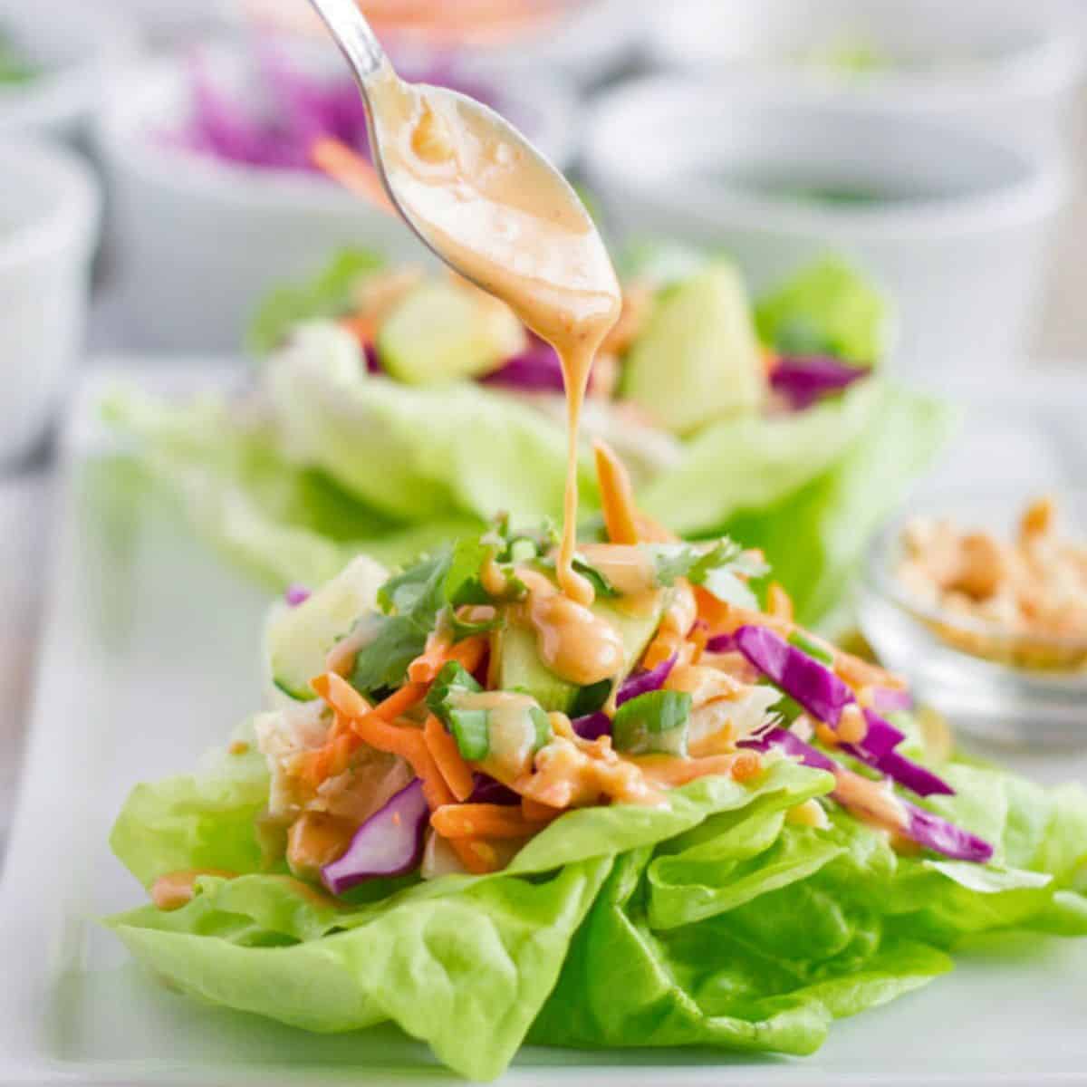 Chicken lettuce wrap with peanut dressing being drizzled on by a spoon.
