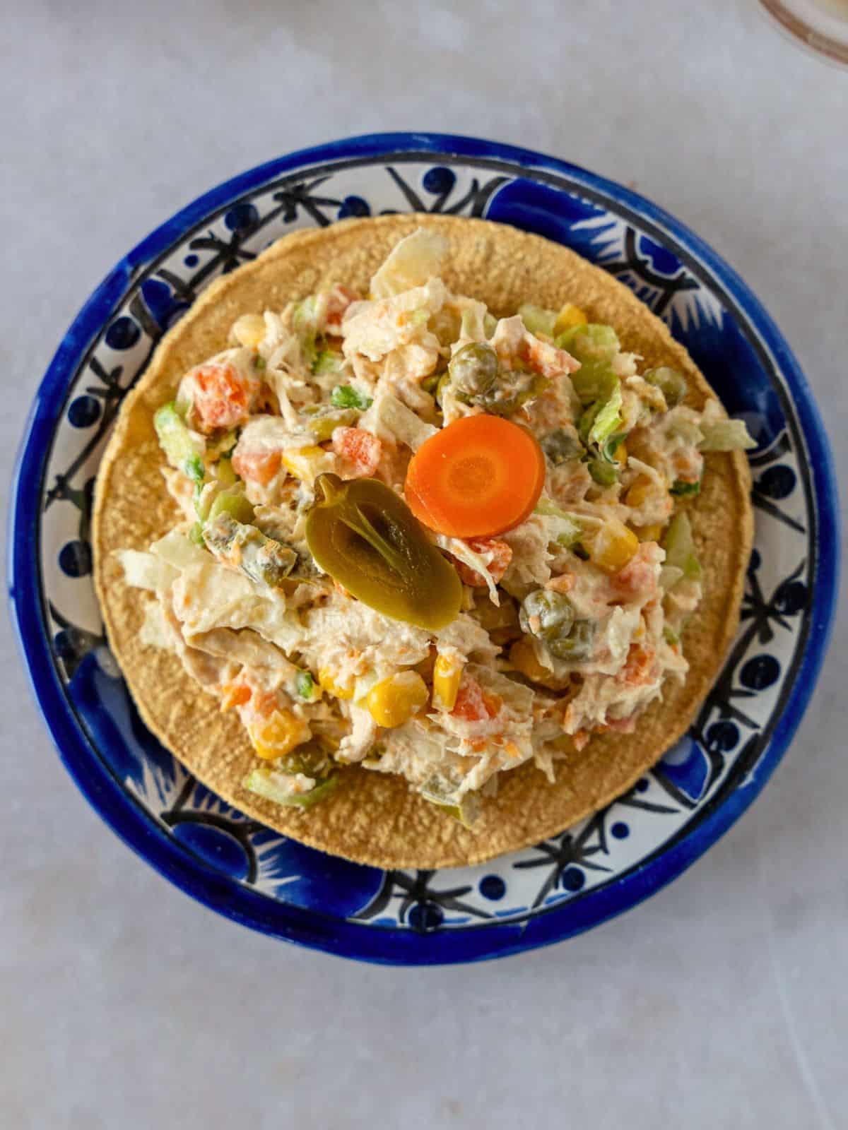 Overhead view Mexican chicken salad on a tostada with a sliced jalapeno and carrot.