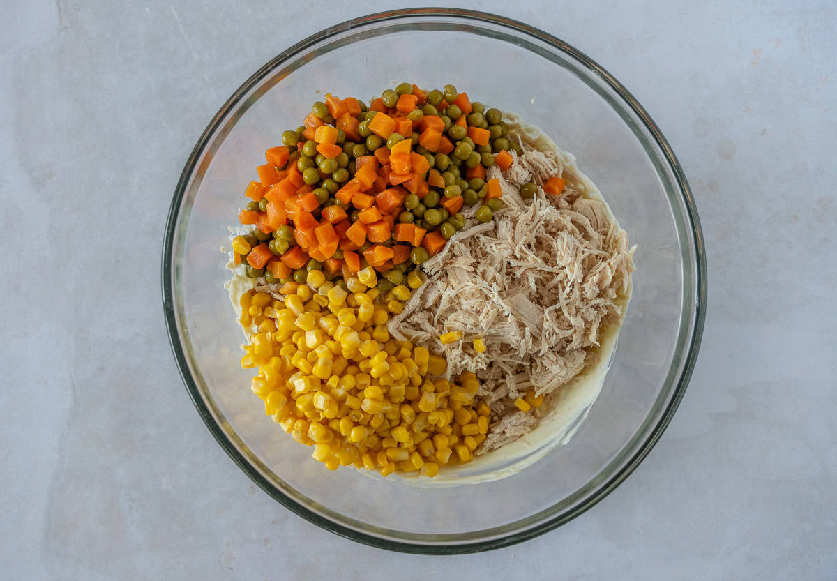 A glass bowl of chicken, corn, peas, and carrots.