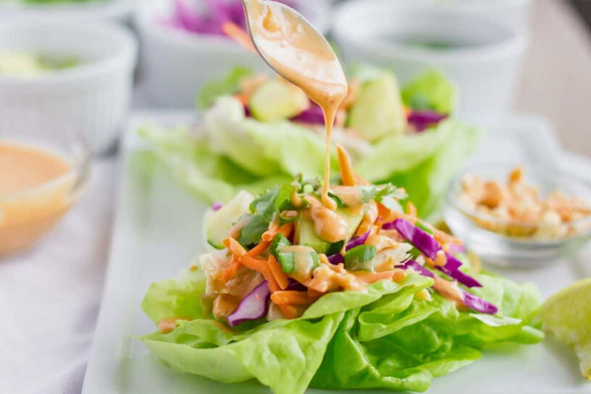 Chicken lettuce wraps with peanut dressing being drizzled on by a spoon.