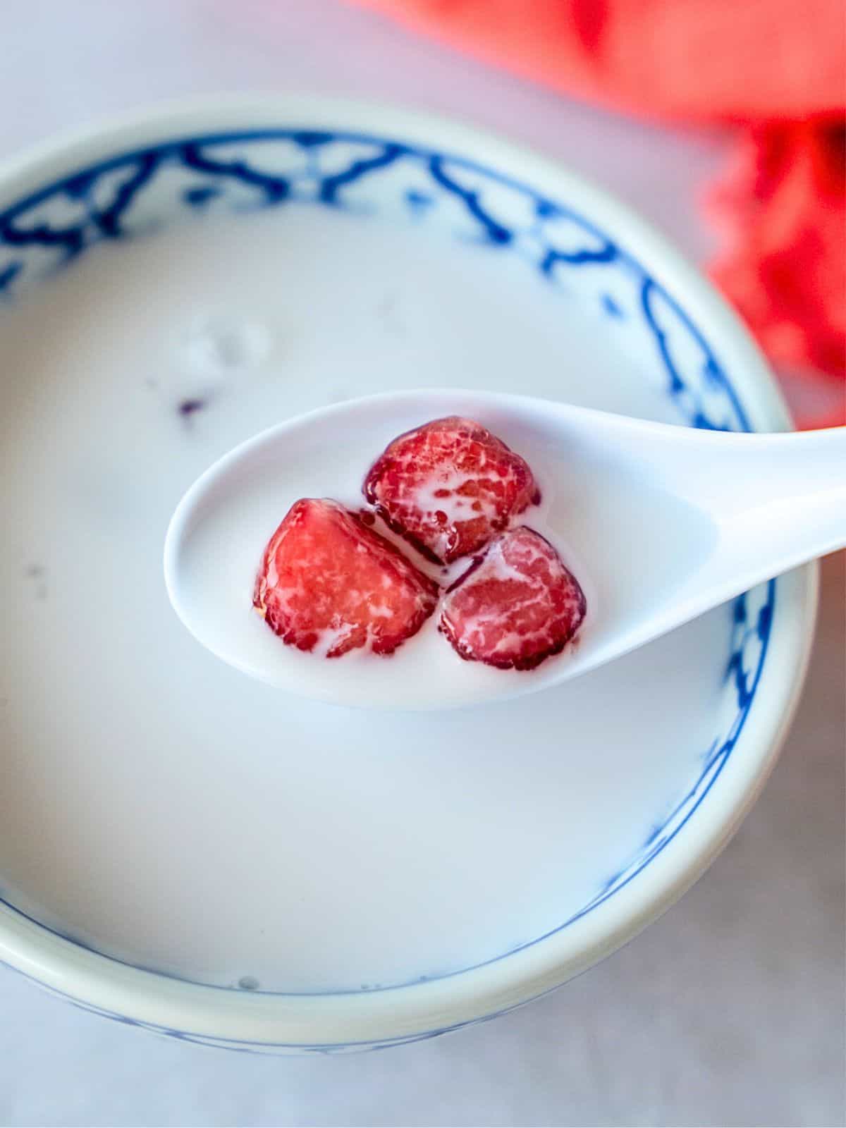 Spoon holding red water chestnuts over coconut milk.