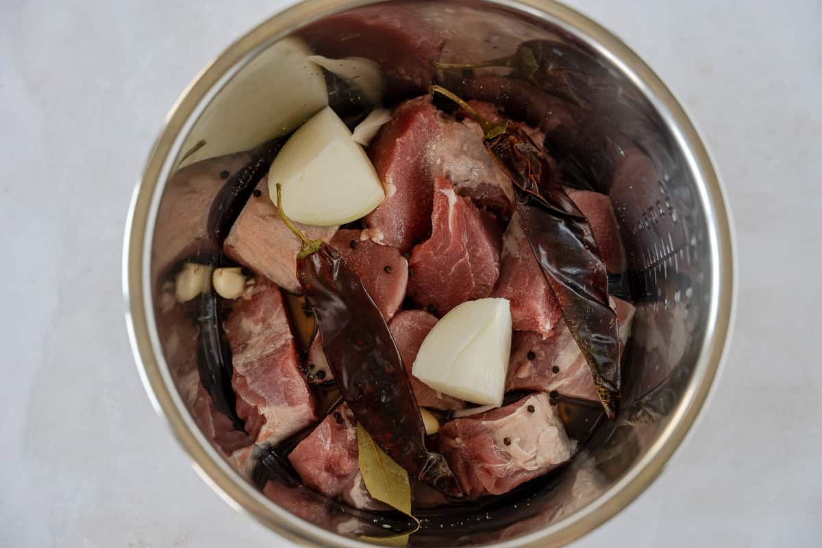 Raw pork, onion, chiles, and peppercorn in a steel pot.