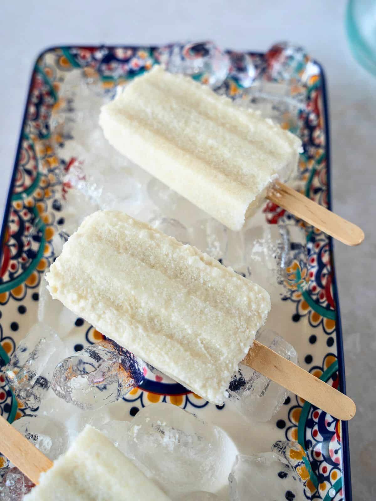Paletas de coco on a plate of ice cubes.