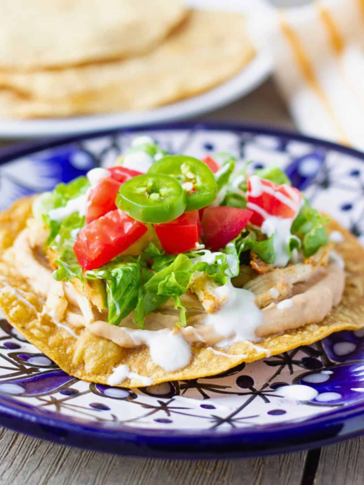 A chicken tostada on a a blue plate with more tostadas in the background.