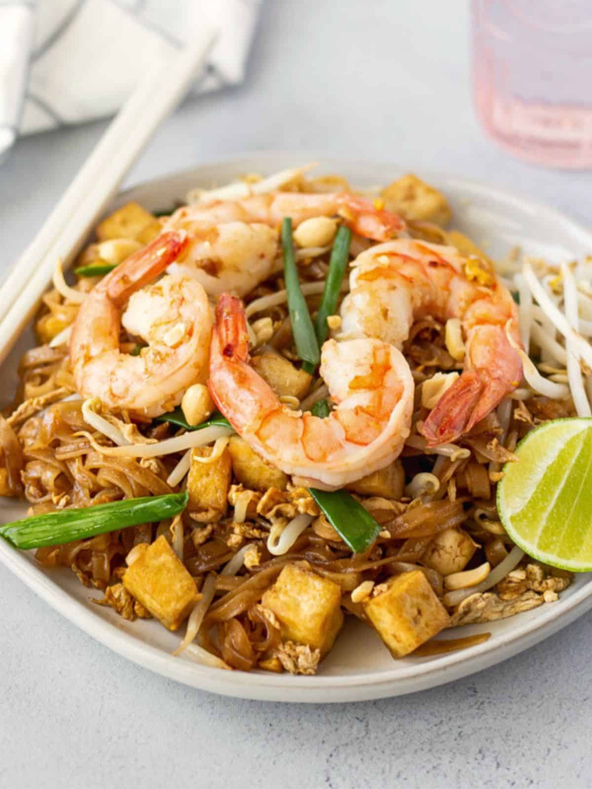 Pad Thai with shrimp and tofu on a plate with lime and bean sprouts.