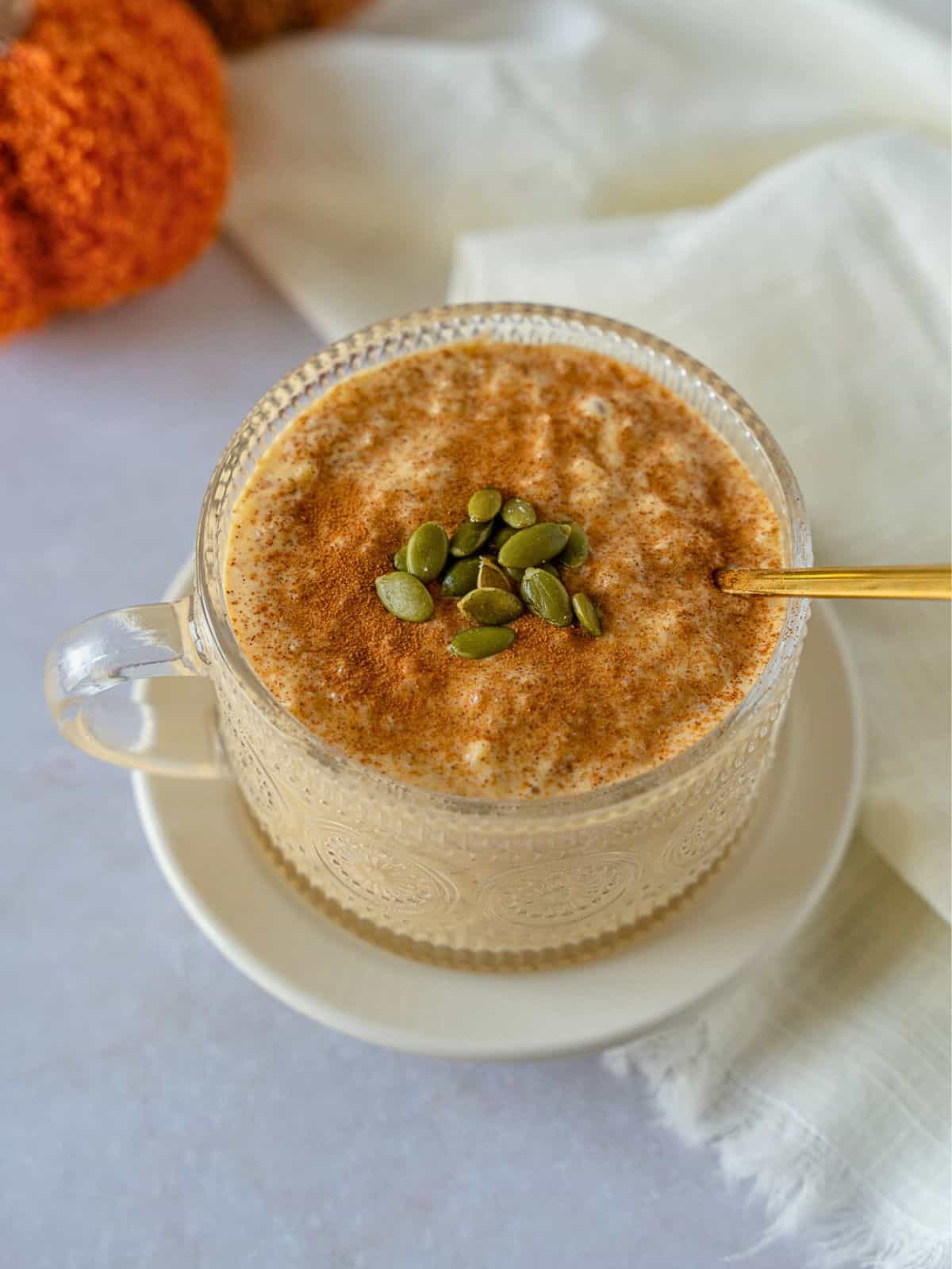 Pumpkin rice pudding in a glass cup topped with cinnamon and pumpkin seeds.