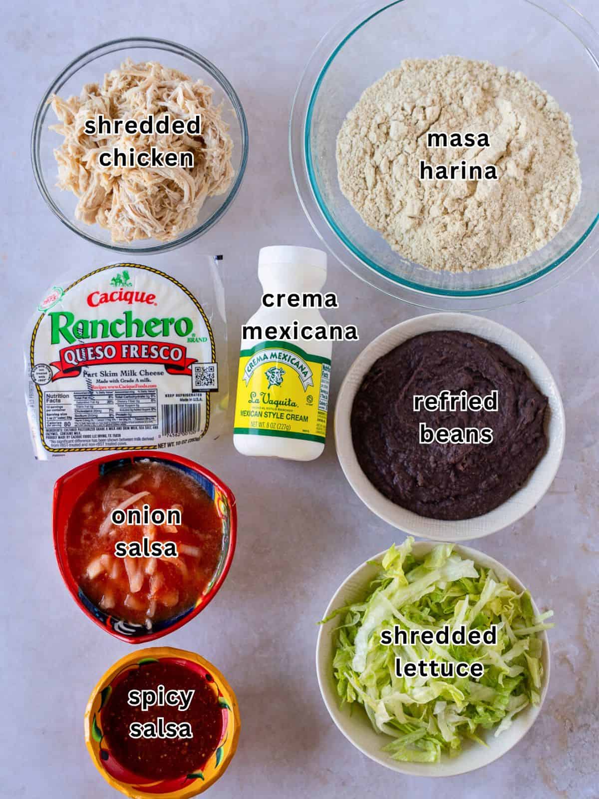 Ingredients with text- shredded chicken masa harina, queso fresco, crema mexicana, refried beans, onion salsa, spicy salsa, and shredded lettuce.