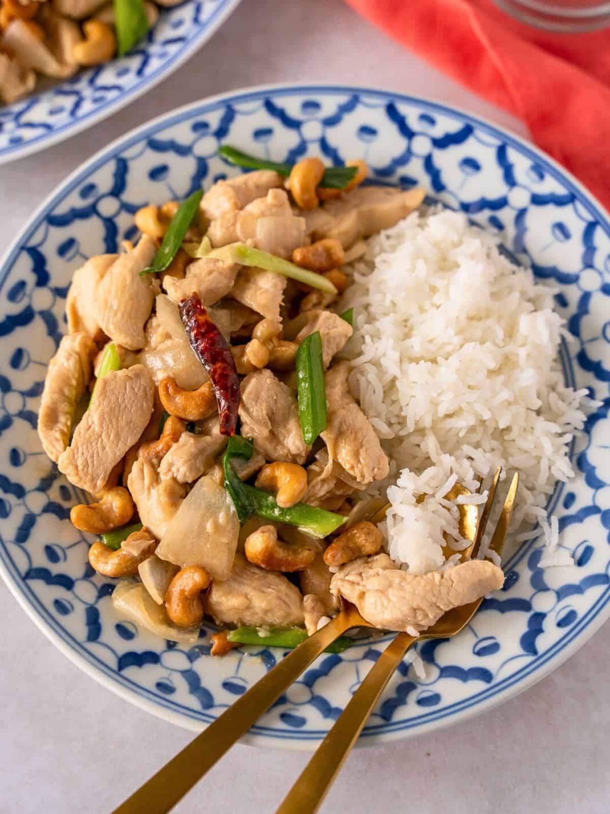Thai cashew chicken with rice on a plate with a gold spoon and fork.