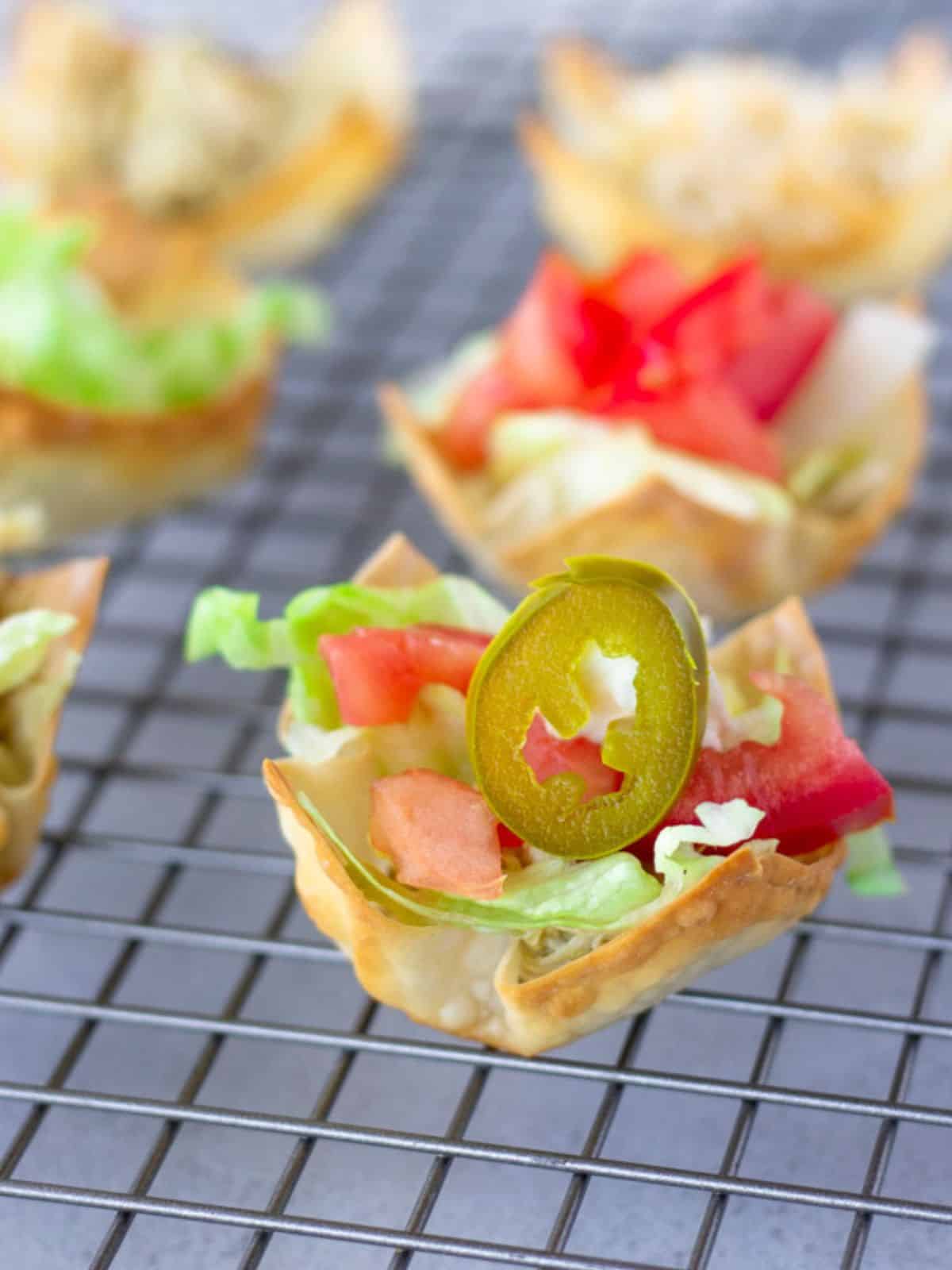 Wonton taco cup with lettuce, tomato, and a jalapeno slice.
