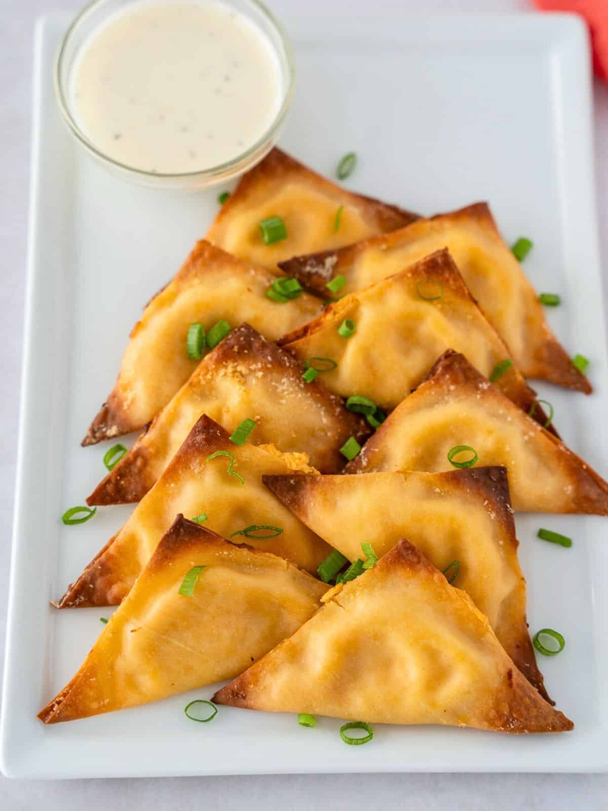 Overhead view of buffalo chicken wontons on a plate with a side of ranch dressing.