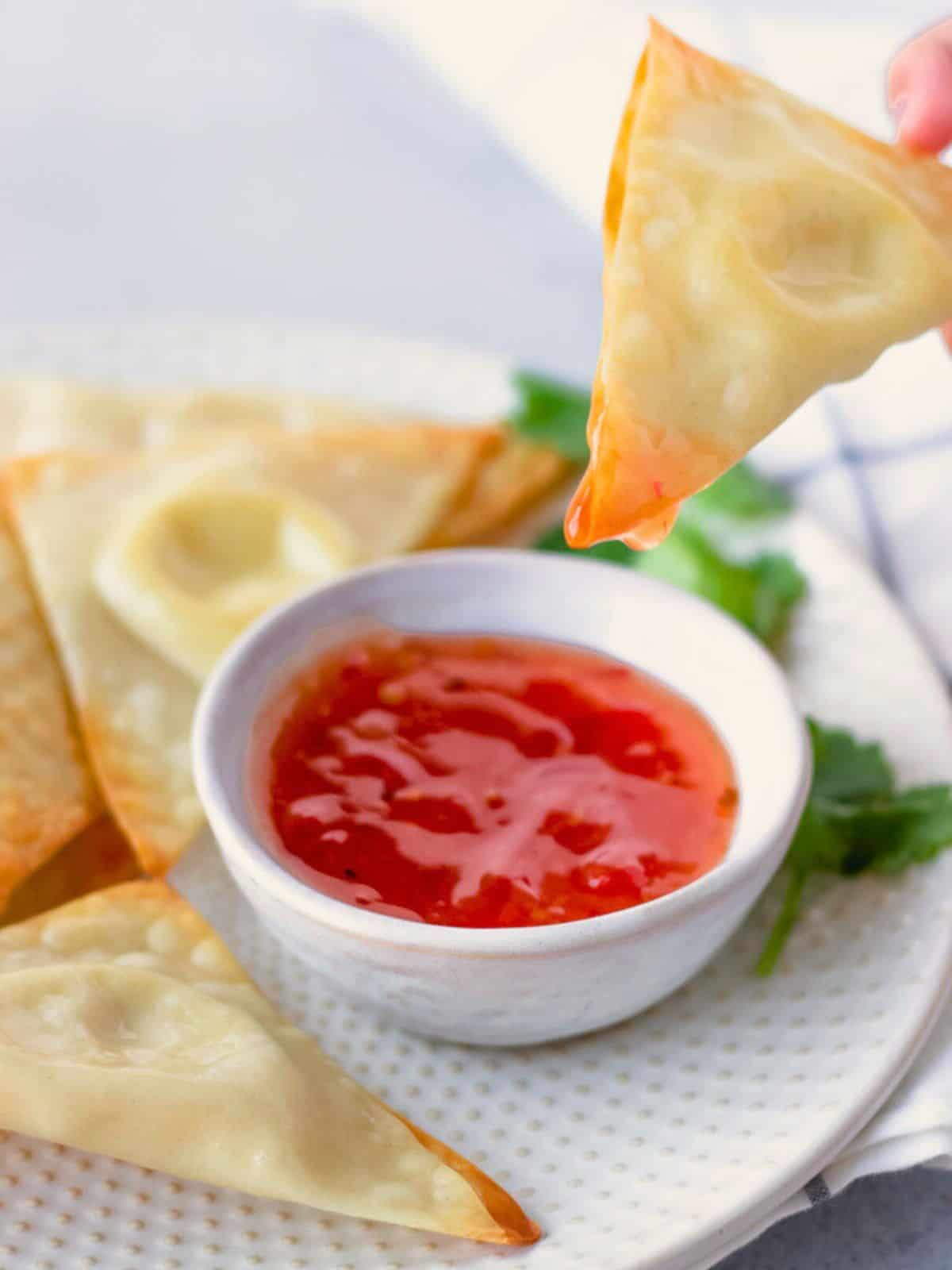 Wonton being dipping in sweet chili sauce.