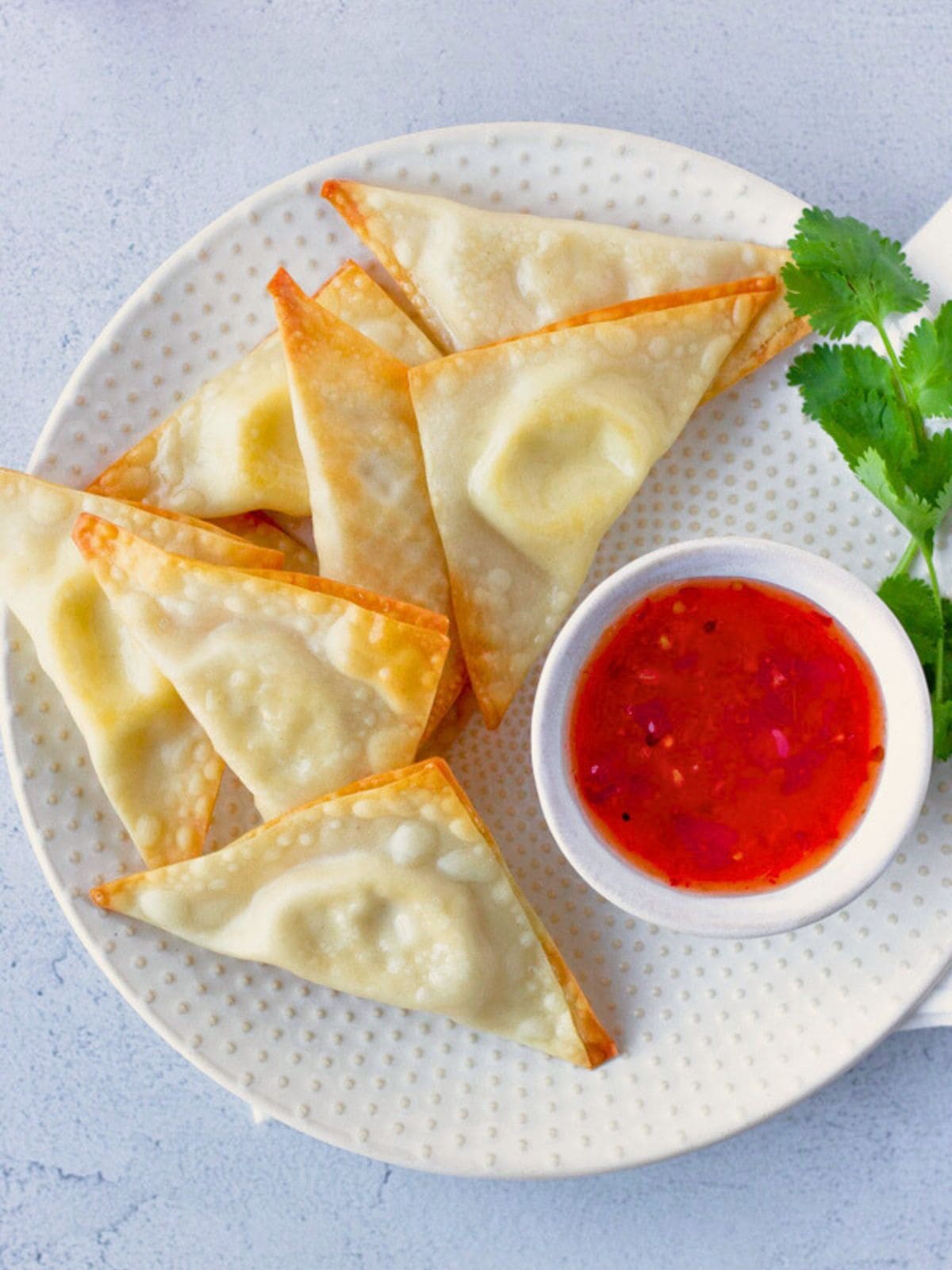 Overhead view of cream cheese wontons on a plate with sweet chili sauce.