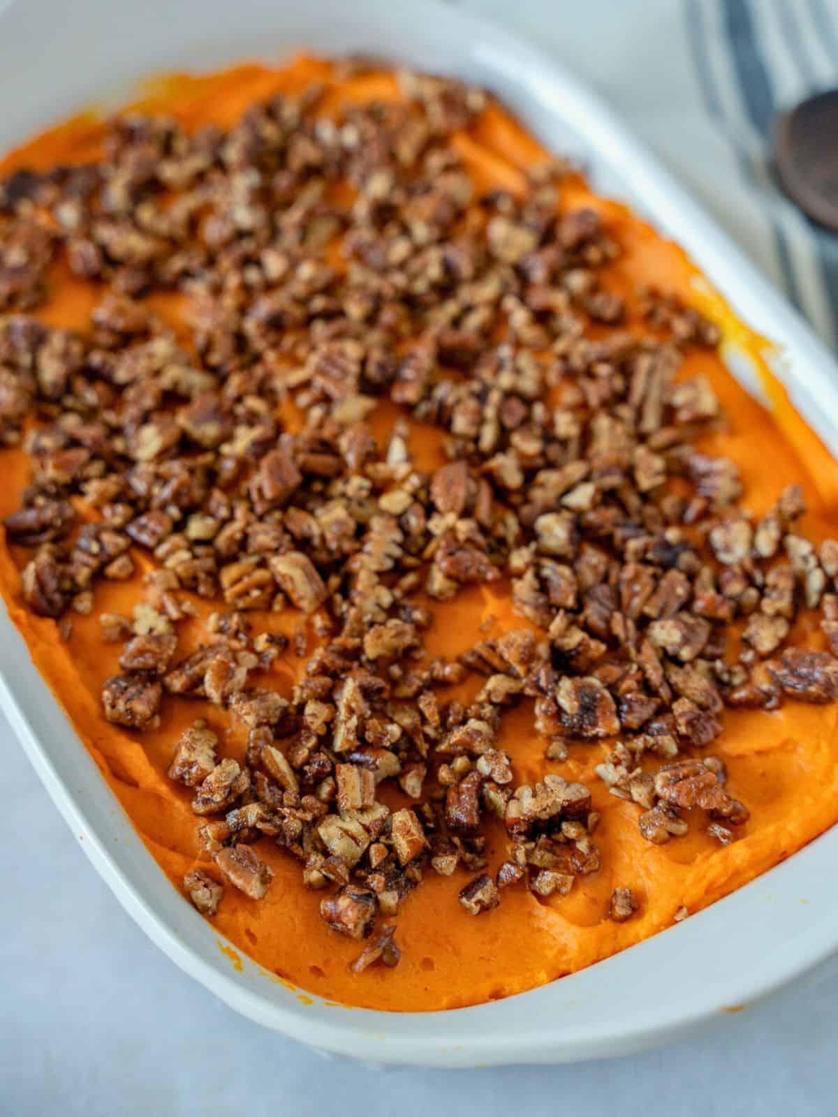 Sweet potato casserole topped with chopped pecans in a white casserole dish.
