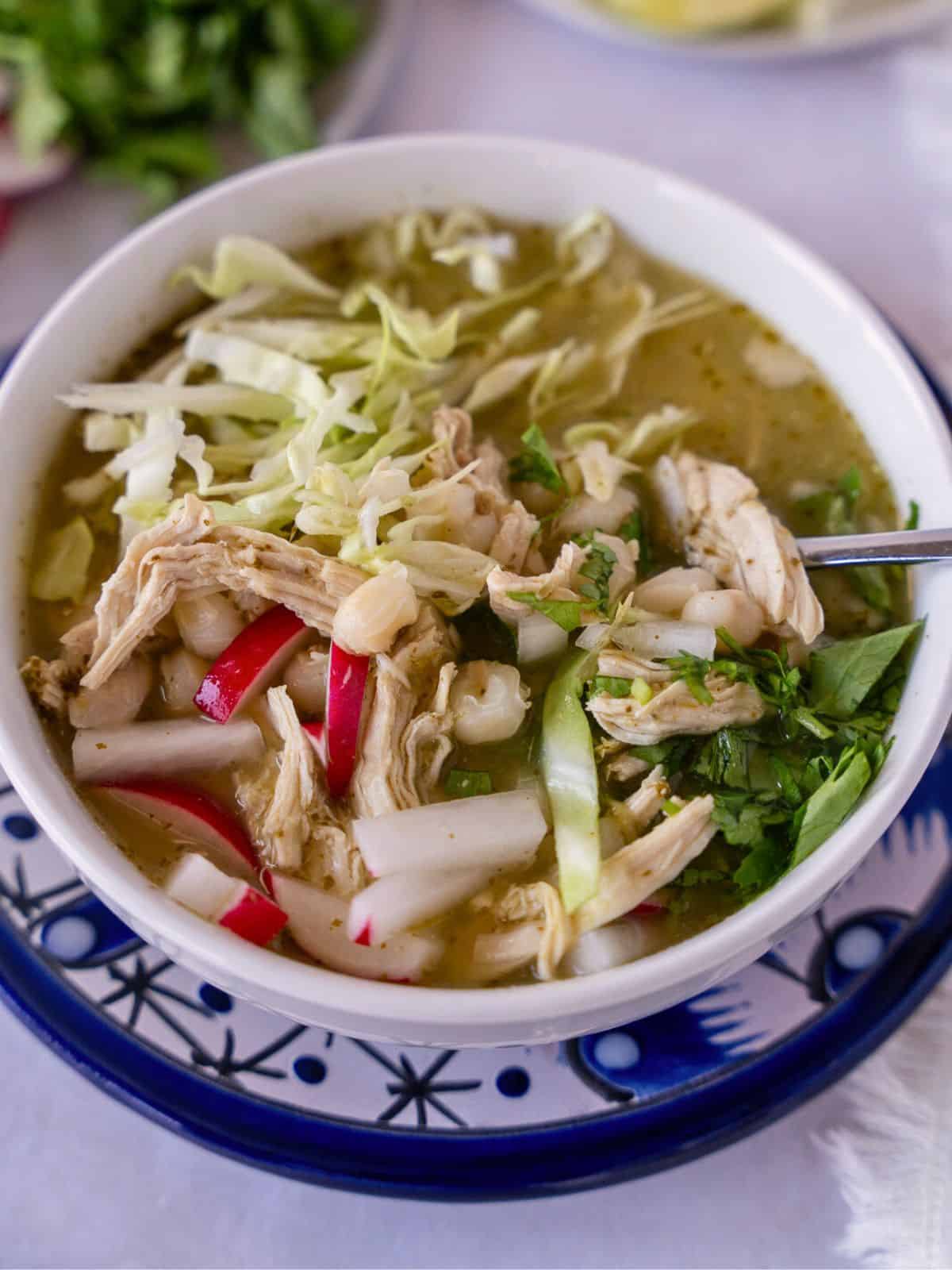 Pozole verde with chicken in a bowl with a spoon.