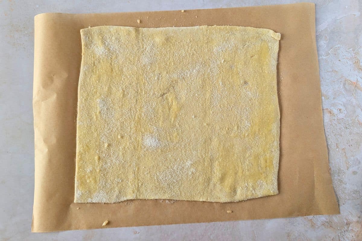 Puff pastry sheet sprinkled with sugar on a piece of parchment paper.