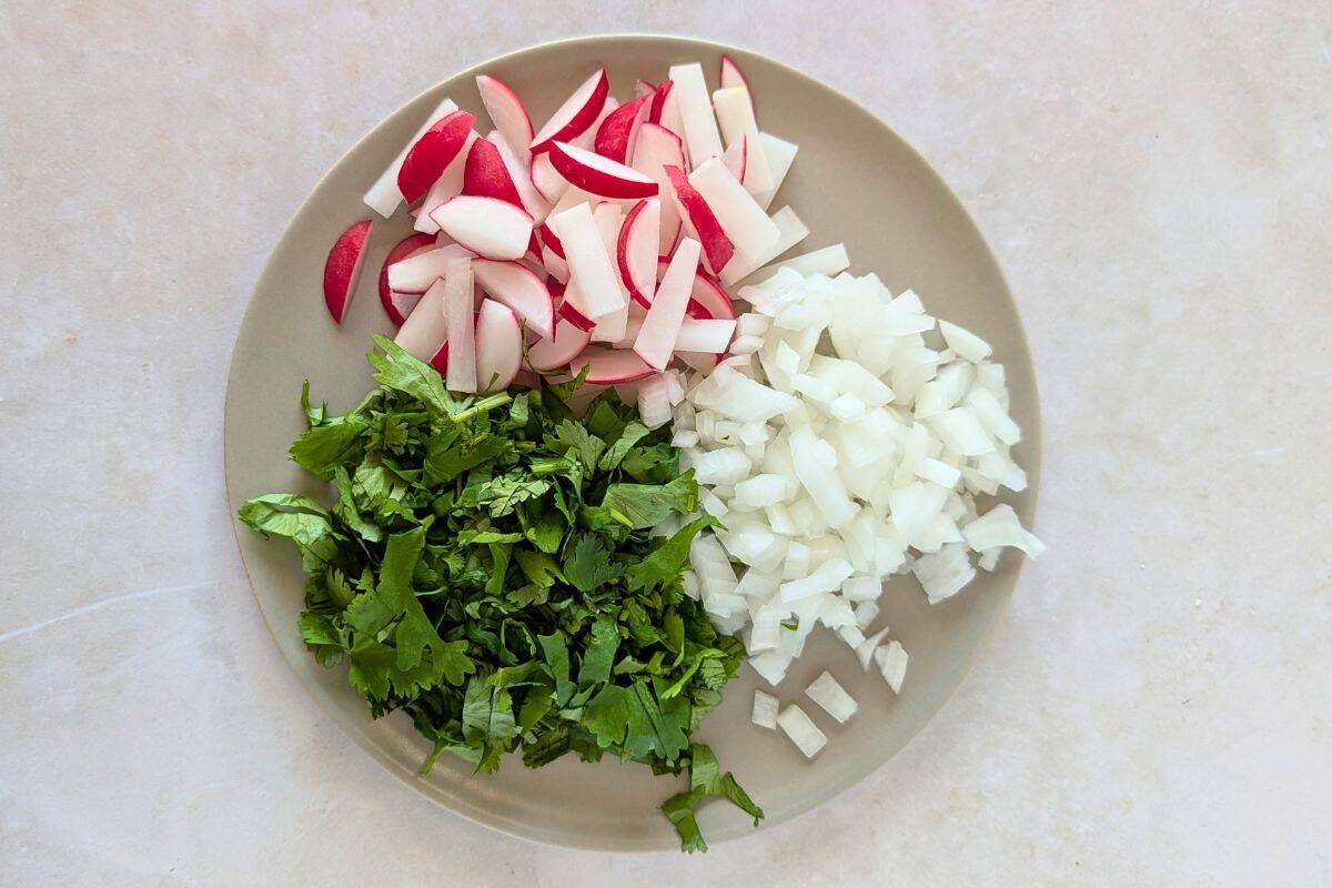 Sliced radishes, cilantro, and chopped onions on a plate.