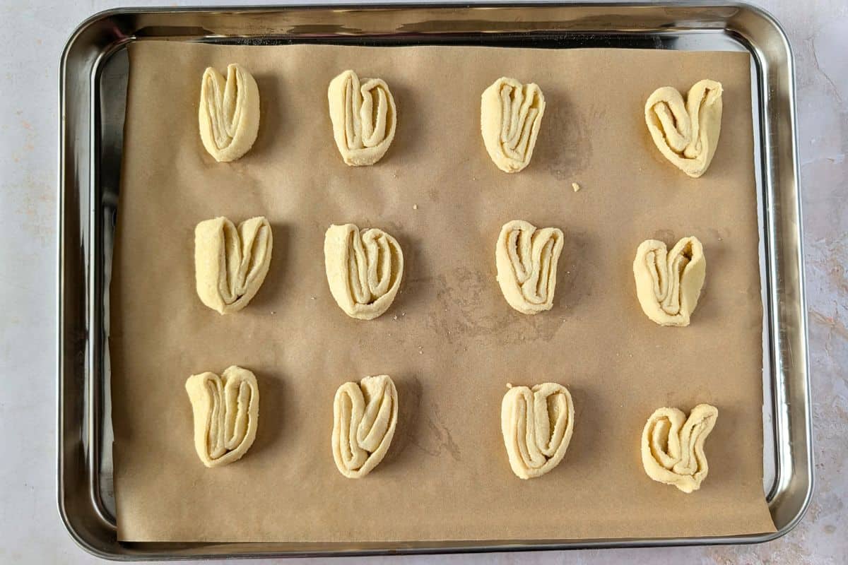 Unbaked orejas on a baking sheet lined with parchment paper.
