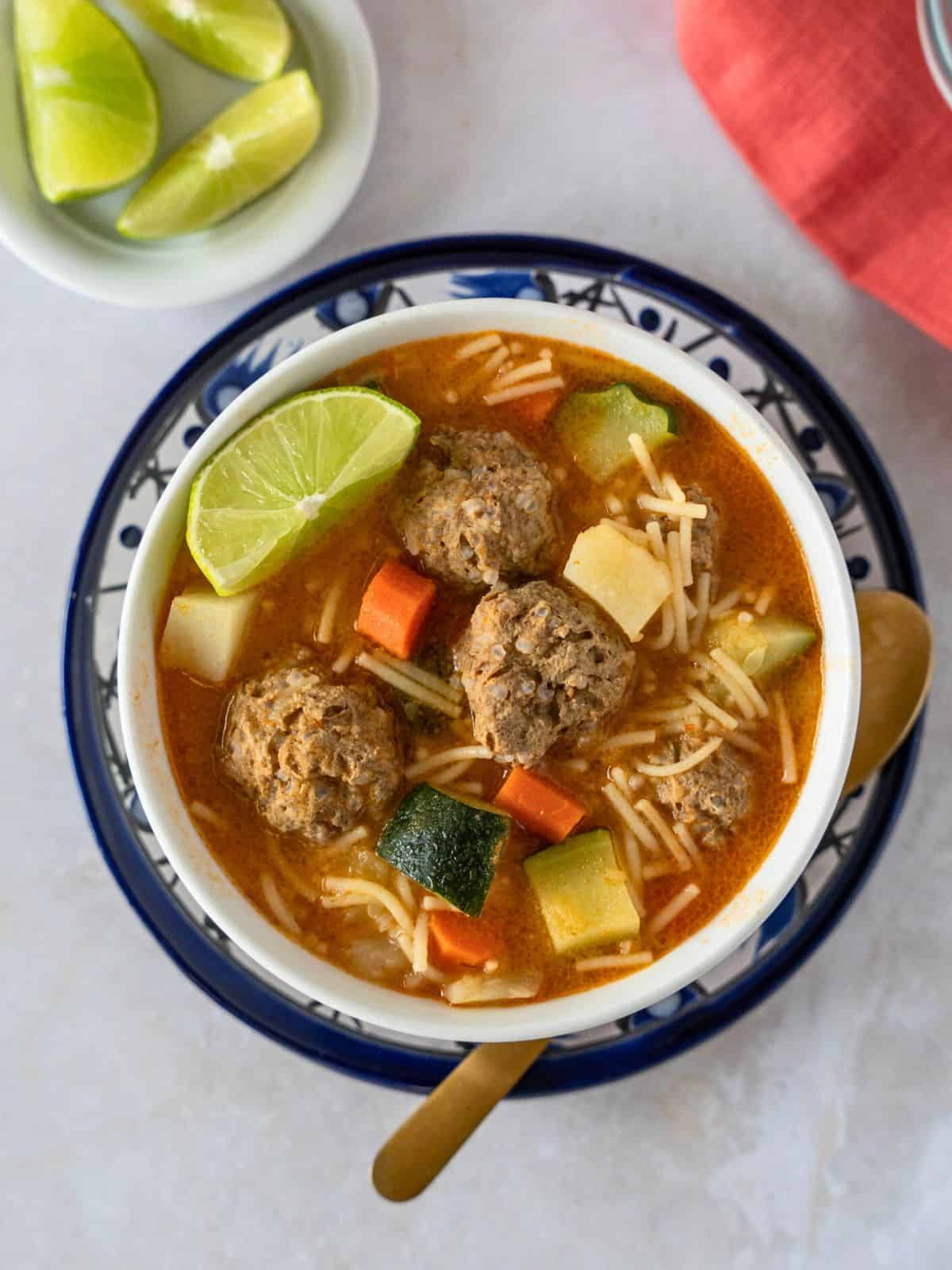 Overhead view of albondigas con fideo in a bowl with lime wedges on the side.