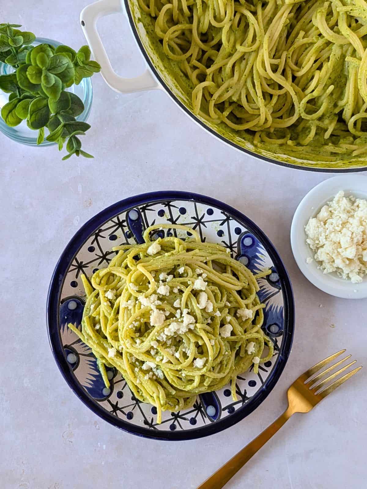 Overhead view of espagueti verde on a blue plate and more in a pan on the side.