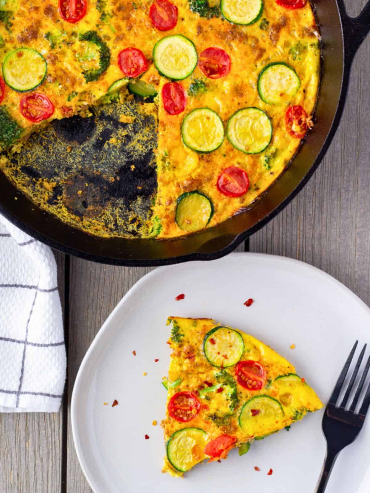 Overhead view of frittata in a cast iron skillet and one slice on a plate.