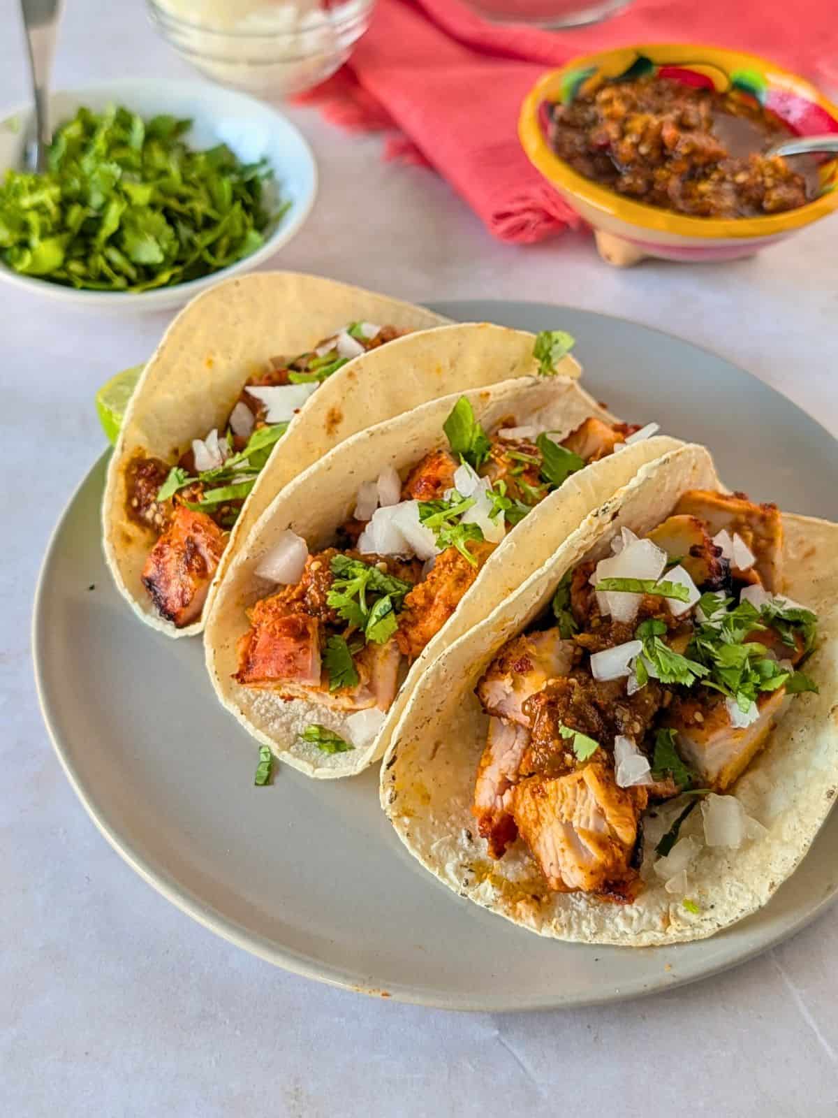 Three pollo asado tacos on a plate topped with salsa, onion, and cilantro.