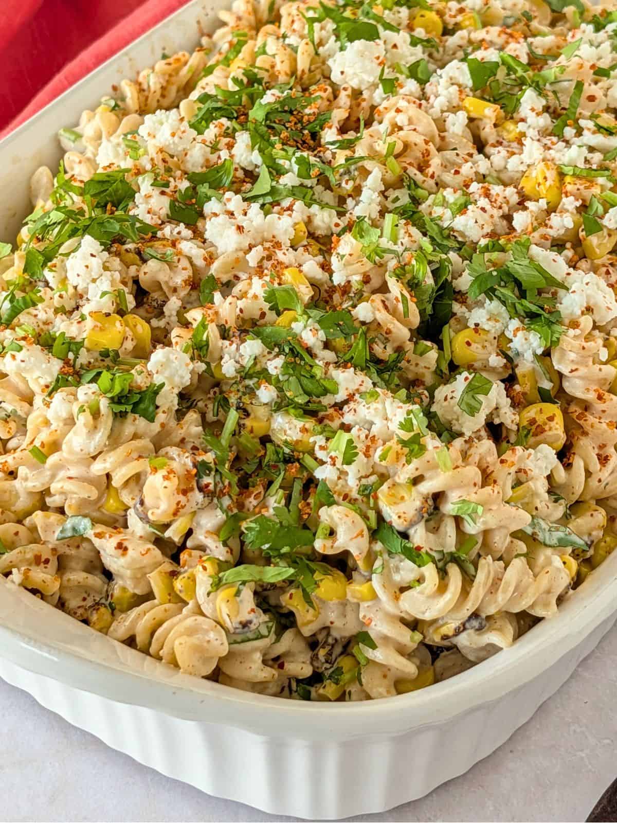 Elote pasta salad in a dish topped with queso fresco, cilantro, and tajin.