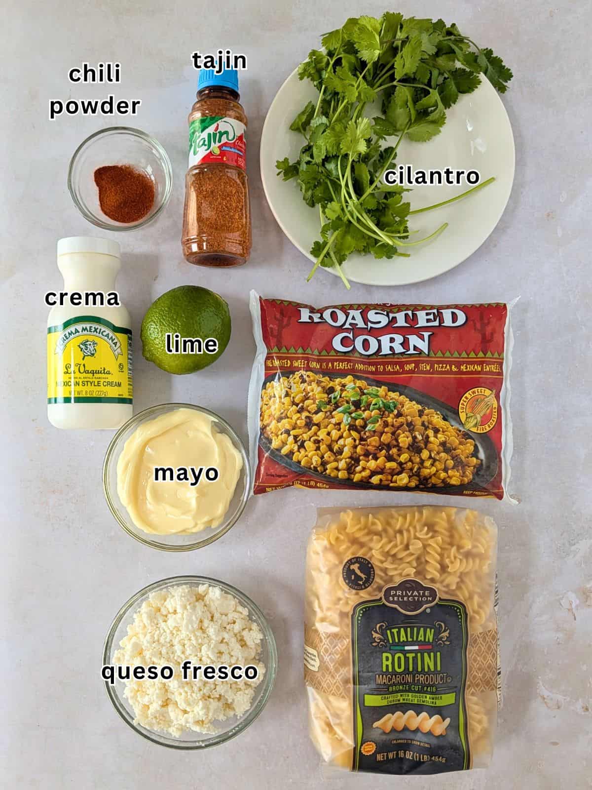 Ingredients with text- chili powder, tajin, cilantro, crema, lime, corn, mayo, queso fresco, and pasta.