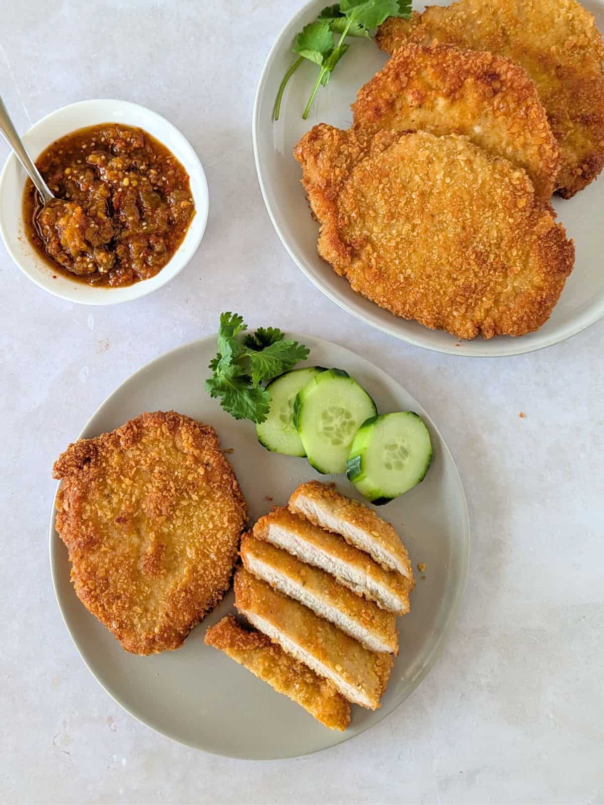 Overhead view of pork milanesa on two plates with a side of salsa.
