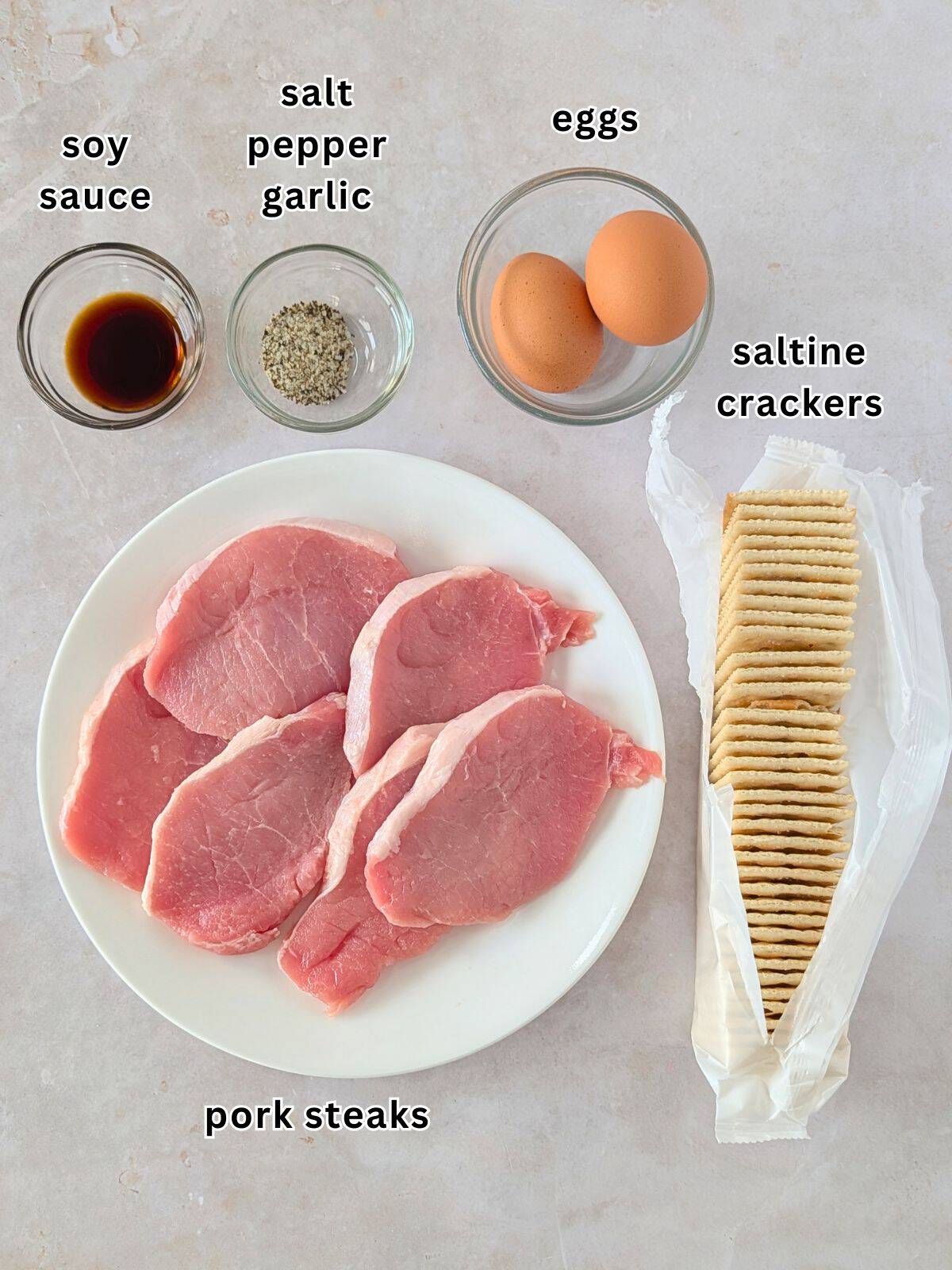 Ingredients with text- soy sauce, salt, pepper, garlic, eggs, saltine crackers, and pork steaks.