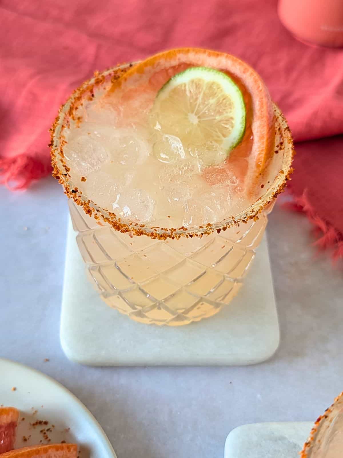 Paloma cocktail in a glass rimmed with chili lime salt.