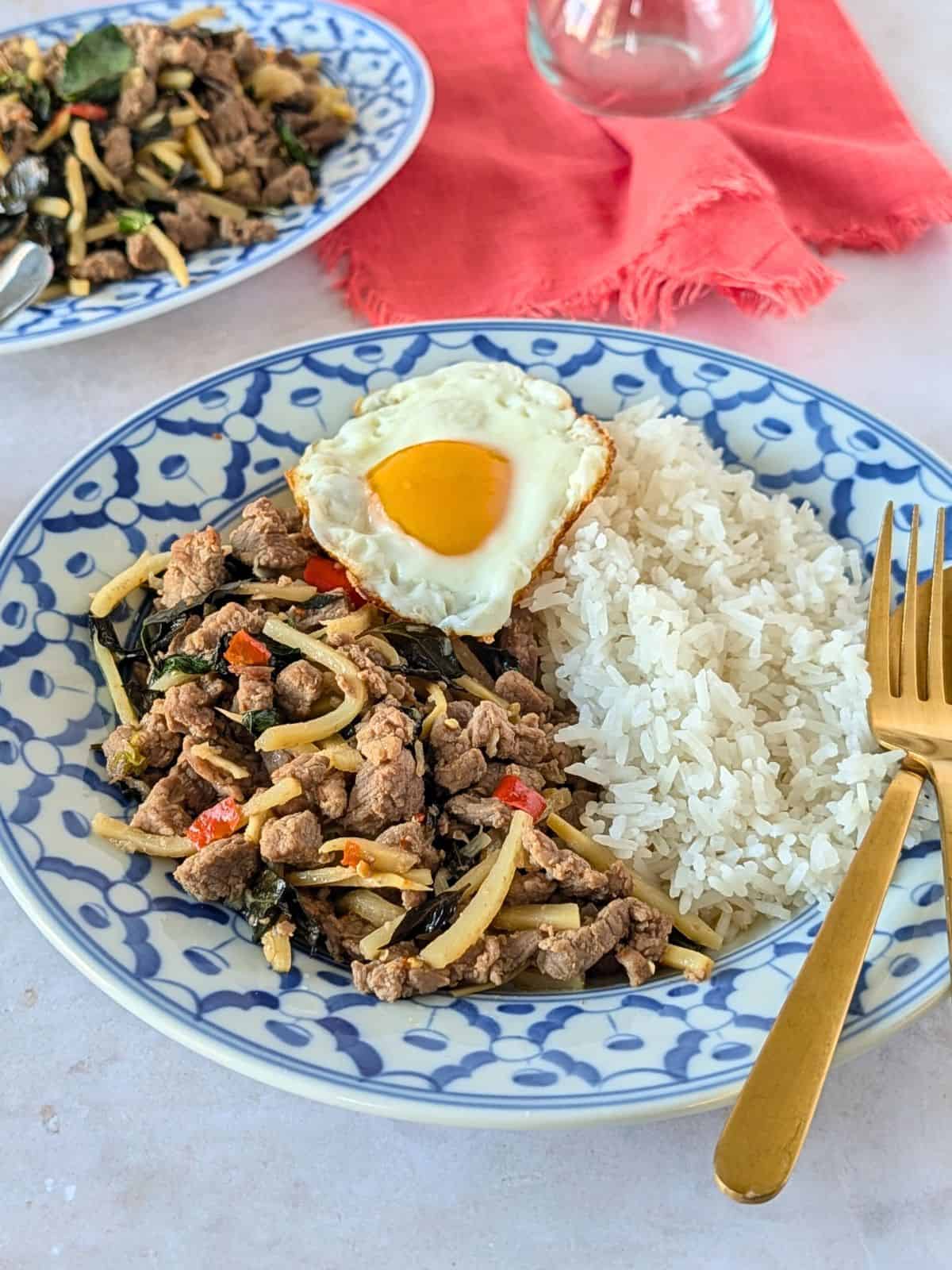 Thai basil beef with bamboo on a blue plate with rice and a fried egg.