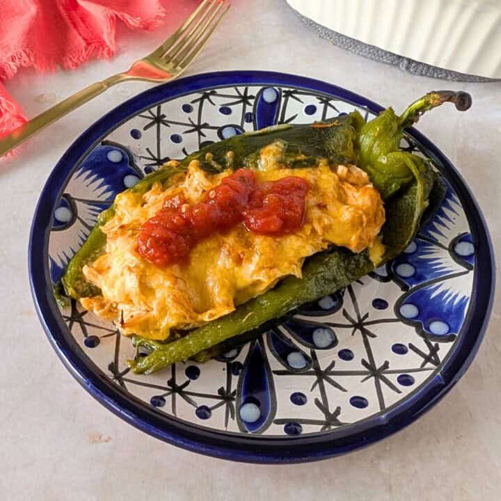 Baked chile relleno stuffed with shredded chicken and topped with melted cheese on a decorative plate.