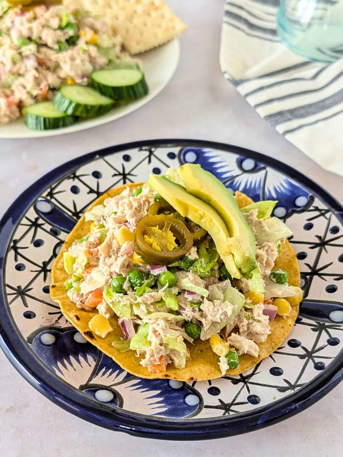 Mexican tuna salad piled on a tostada and garnished with avocado and jalapeno slices.