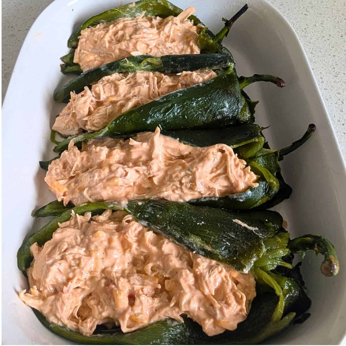 Roasted poblano peppers stuffed with a creamy shredded chicken filling before baking.