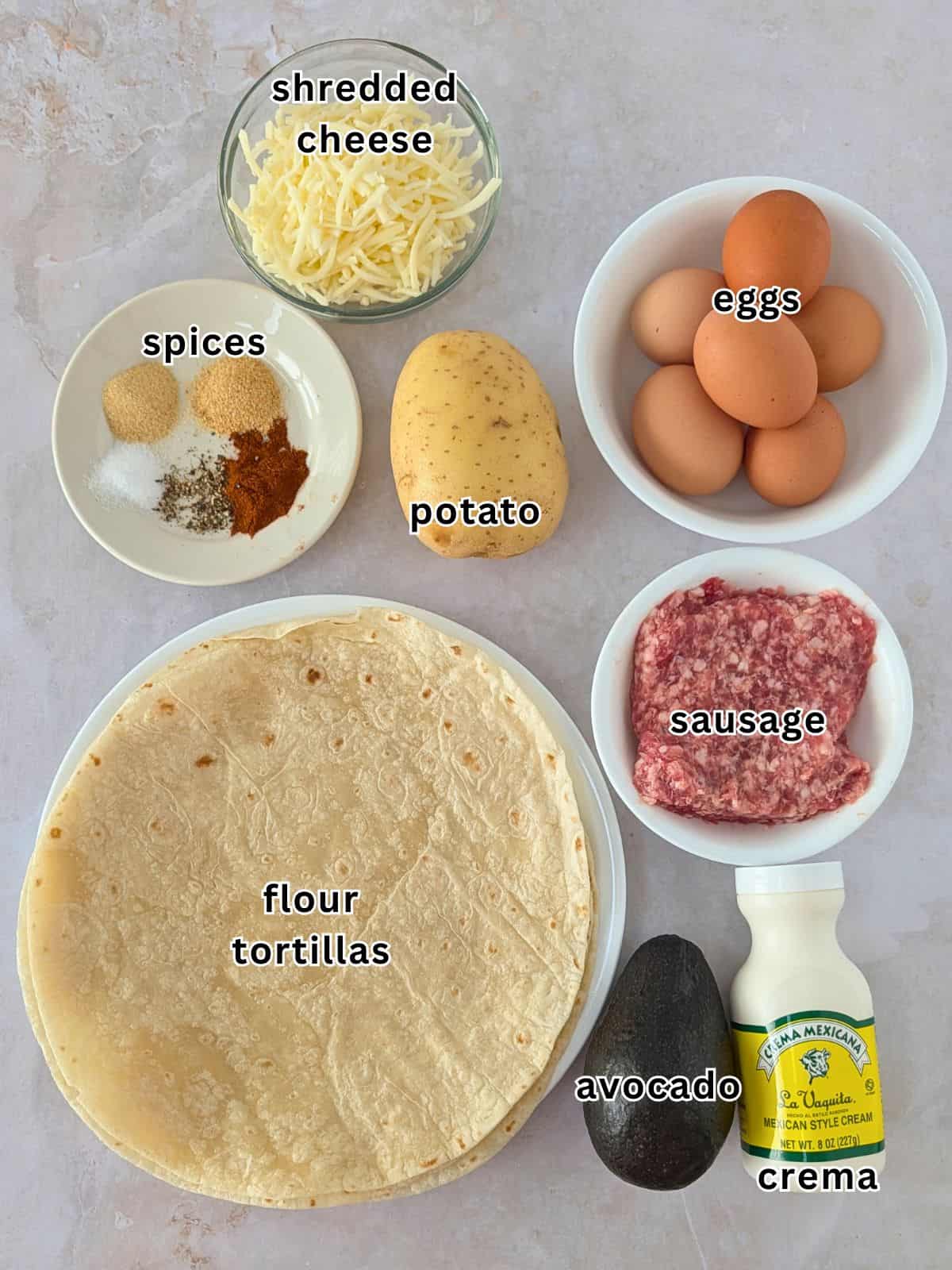 Ingredients with text- shredded cheese, eggs, spices, potato, sausage, flour tortillas, avocado, and crema.
