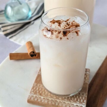 Feature image of horchata in a glass with a cinnamon stick on the side.