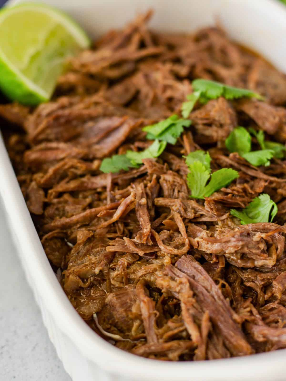 Shredded beef in a dish topped with cilantro and a lime wedge.