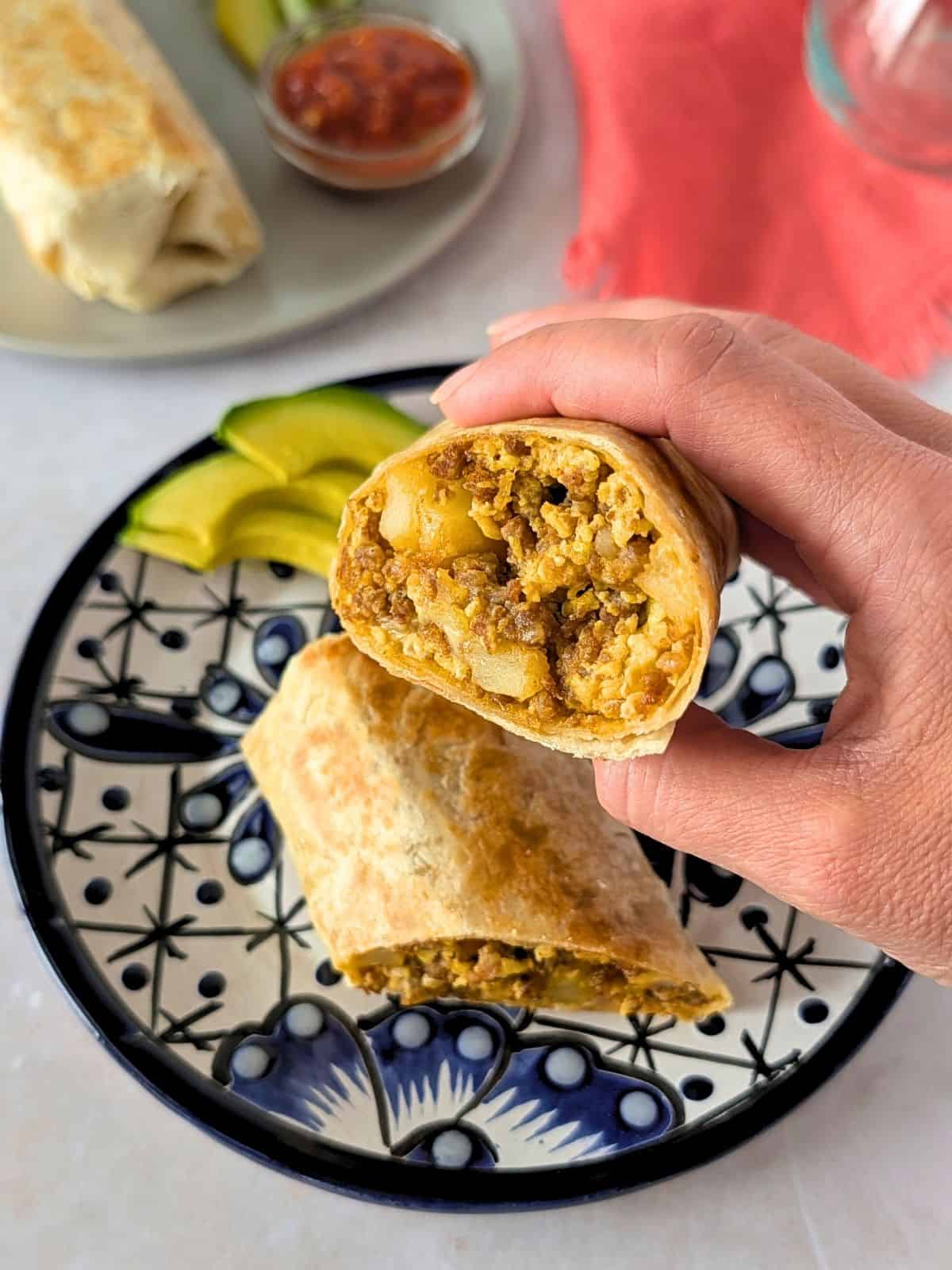 A hand holding a chorizo burrito over a blue plate.