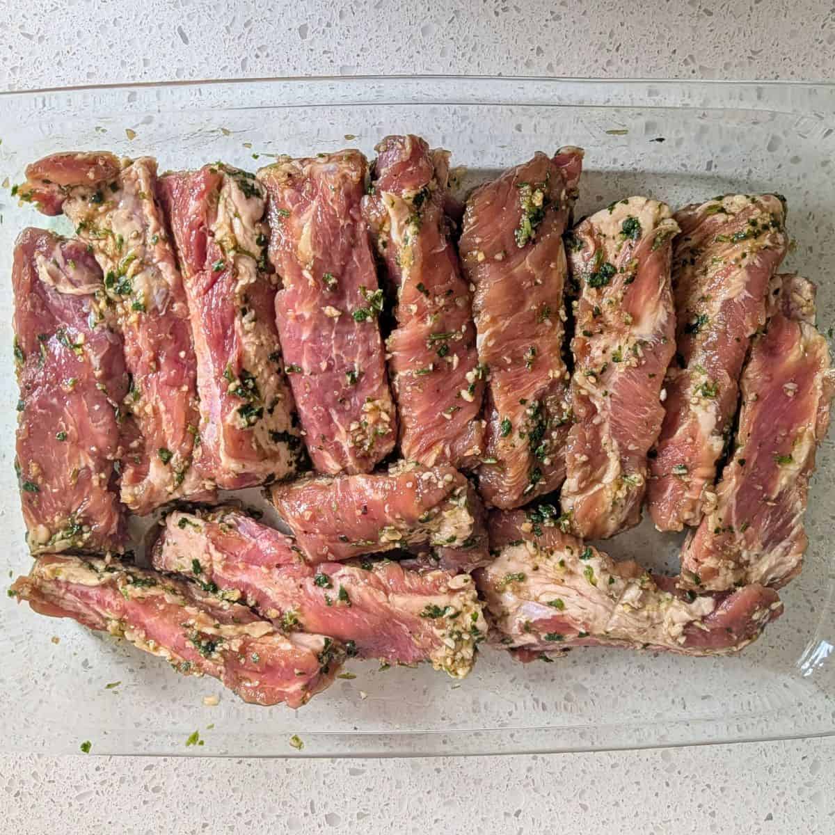 Uncooked marinated ribs in a glass baking dish.