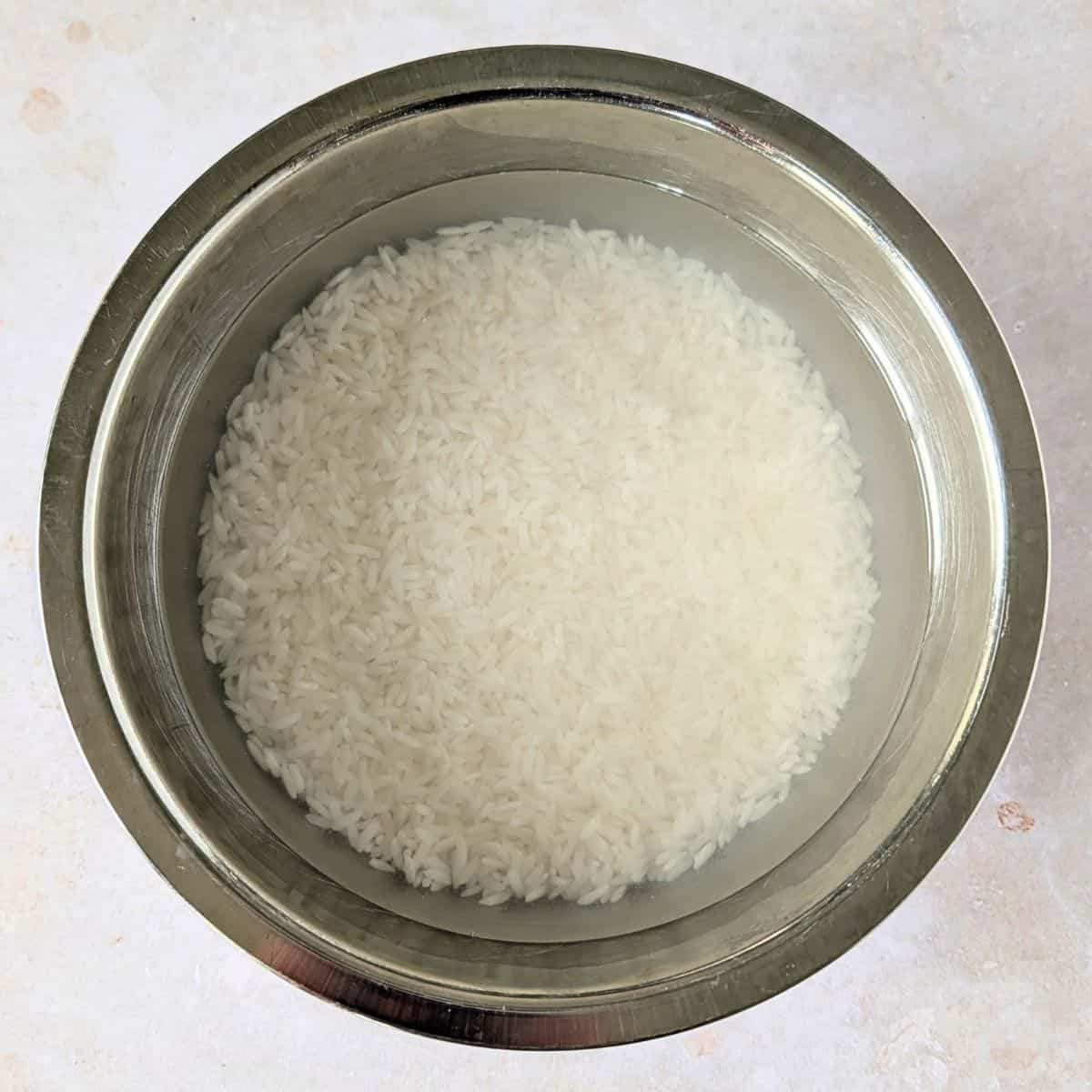Rice soaked in water in a silver bowl.