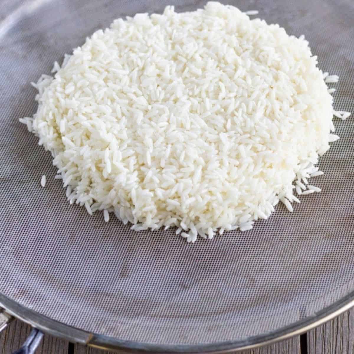 Rice in a flattened mound over a splatter guard and skillet.