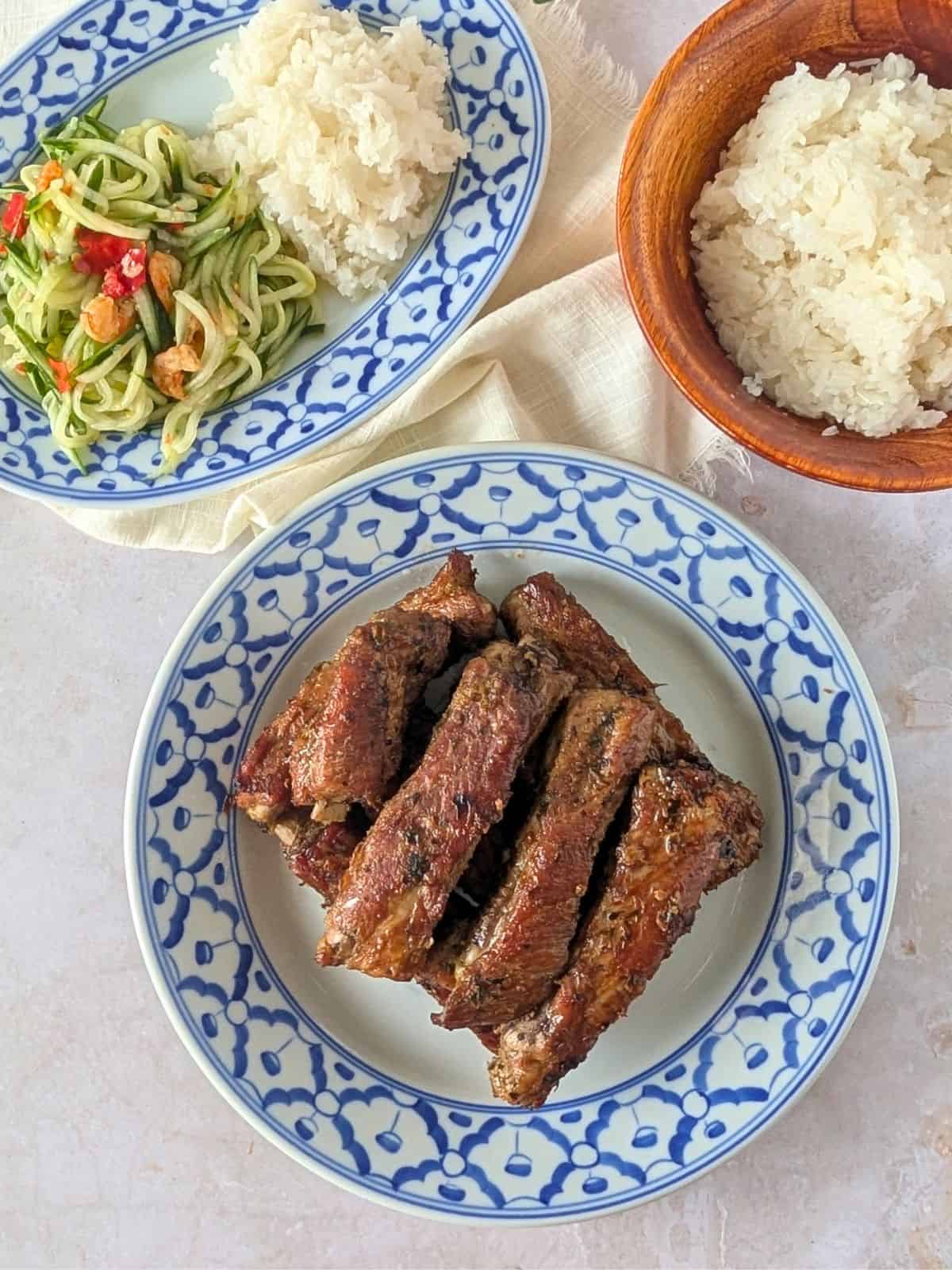 Overhead view of Thai ribs on a plate, with a side of rice, and cucumber salad.