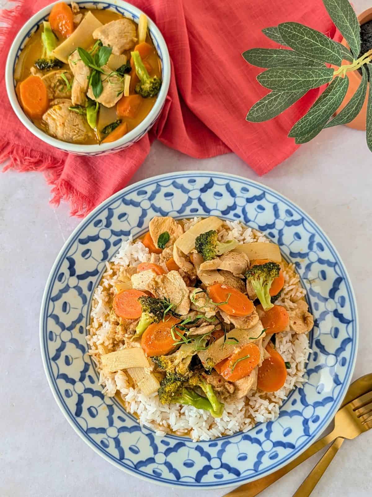 Overhead view of red curry on a plate of rice and a small bowl on the side.